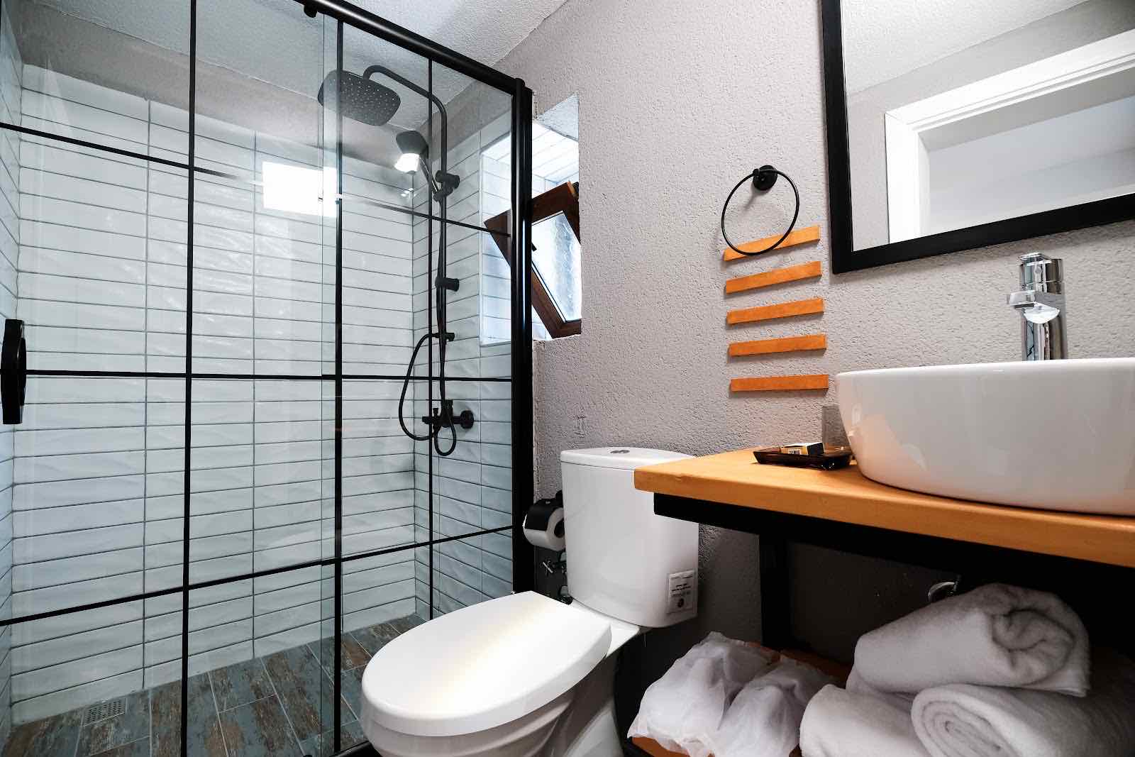 Siyah çerçeveli cam duşakabinli banyo, ahşap tezgâh ve çanak lavabo